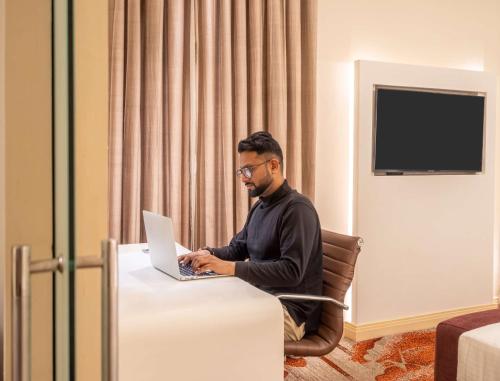 a man sitting at a table with a laptop at Park Plaza Faridabad in Faridabad