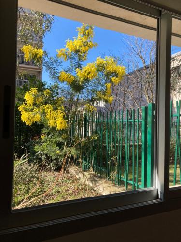 een raam met uitzicht op een boom met gele bloemen bij Vue sur jardin, 3 pièces in Parijs
