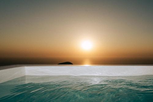 a swimming pool with a sunset in the background at Gazelle Living in Imerovigli