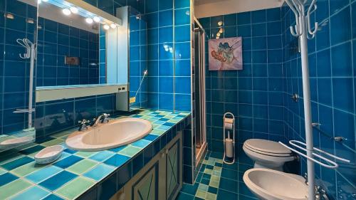 a blue tiled bathroom with a sink and a toilet at Appartamento Emerald in Abbiadori