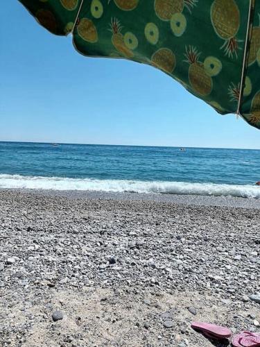 a beach with an umbrella and flip flops on the sand at IL FARO Comfort a 500 m dal mare in Casa Borgorosso