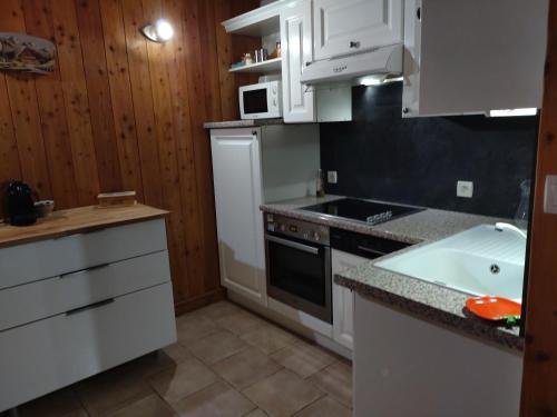 La cuisine est équipée de placards blancs, d'une cuisinière et d'un évier. dans l'établissement CHALET MONTAGNE CLASSÉ 3 ETOILES ALPES QUEYRAs, à Guillestre