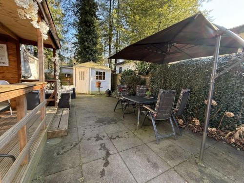 a patio with a table and chairs under an umbrella at VELUWE CHALET HOENDERLOO Private Jacuzzi, Park Swimming Pool and Children's Entertainment in Hoenderloo