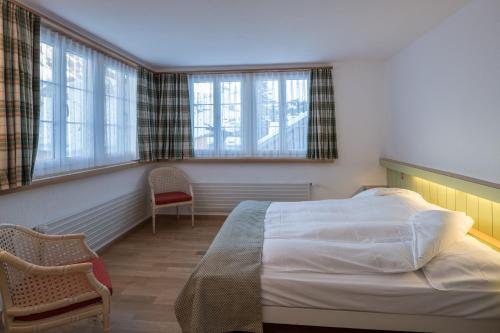 a bedroom with a bed and a chair and windows at Hotel Post in Bivio