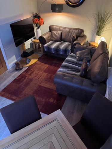 a living room with a leather couch and a tv at Millstone Stables Cottage in Chinley
