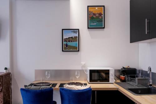 Il comprend une cuisine équipée d'un bureau, d'un four micro-ondes et de chaises bleues. dans l'établissement Le Cocon Villeneuve - hyper center - Clim&Wifi, à Villeneuve-sur-Lot