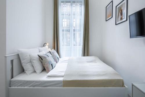 Un dormitorio blanco con una cama con almohadas y una ventana en New Studio Top Location, en Budapest