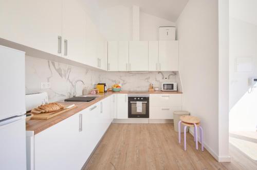 a white kitchen with white cabinets and a wooden floor at Ocean & Sun Terrace w AC, by TimeCooler in Costa da Caparica