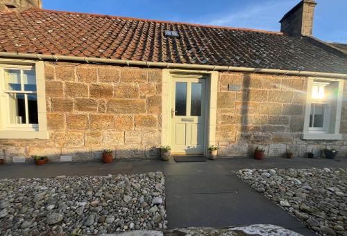 a stone house with a yellow door and a gravel driveway at Beach Cottage in a Tranquil Location in Kingsbarns