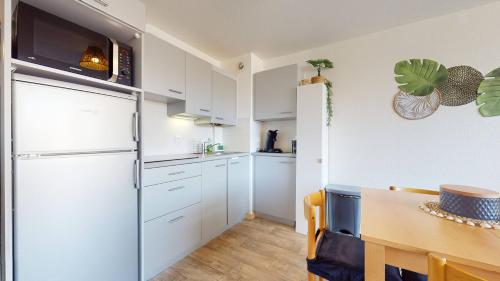 - une cuisine avec des placards blancs, une table et un réfrigérateur dans l'établissement Studio Cabine avec Piscine et Place de parking privée CAP D'AGDE, au Cap d'Agde