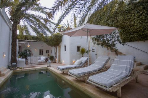a swimming pool with lounge chairs and an umbrella at La Maison Blanche -Les Houchs De Djerba in Erriadh