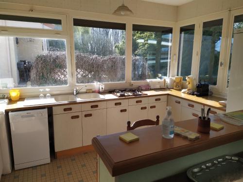 une cuisine avec des placards blancs, une table et des fenêtres dans l'établissement La maison du pêcheur, à Saint-Martin-de-Sanzay