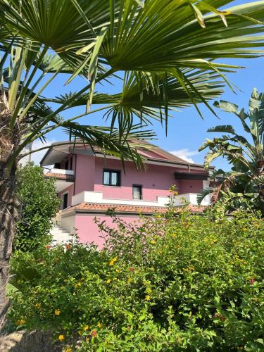 a pink building behind some trees and bushes at Villa Cocomerara Tas24 in Calimera