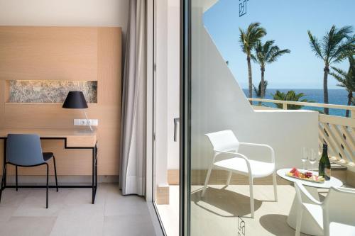 a room with a desk and a balcony with the ocean at Plus Fariones Suite Hotel in Puerto del Carmen