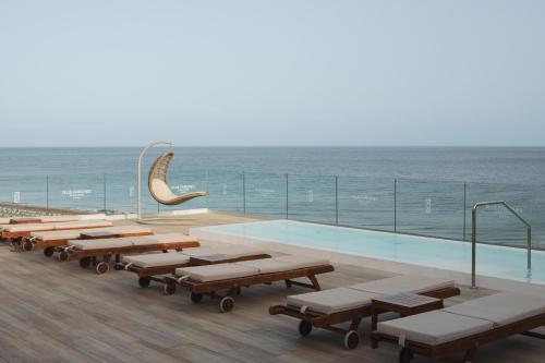 a pool with benches and the ocean in the background at Plus Fariones Suite Hotel in Puerto del Carmen