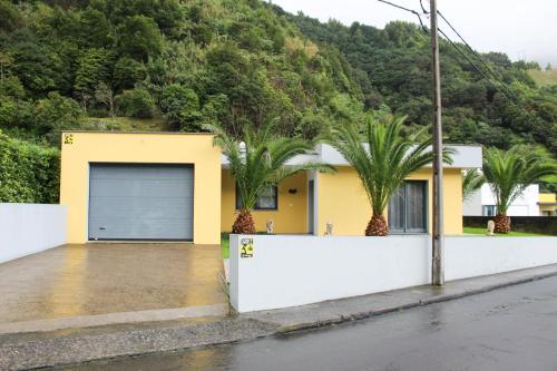 a yellow house with a garage and palm trees at Waterfall House in Faial da Terra