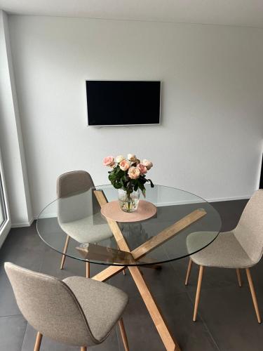 a glass table with chairs and a vase of flowers at Neue helle Wohnung mit Bergblick am Eingang der Jungfrau Region und Berner Oberland in Aeschi bei Spiez