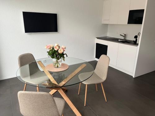 a glass table with chairs and a vase of flowers at Neue helle Wohnung mit Bergblick am Eingang der Jungfrau Region und Berner Oberland in Aeschi bei Spiez