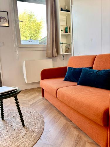 an orange couch in a living room with a window at Le Petit Chai - Studio tout equipé au calme proche universités et transports in Talence