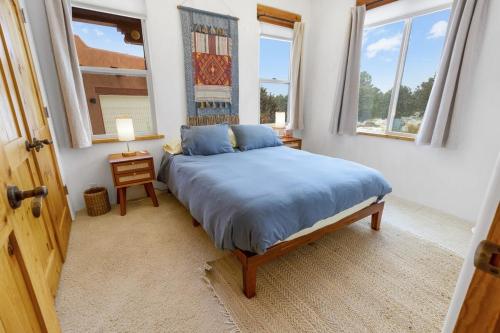 a bedroom with a bed with blue sheets and two windows at Crestone Adobe Vista Manor in Crestone
