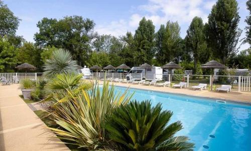 - une piscine avec des chaises longues et des palmiers dans un complexe dans l'établissement Camping 3 étoiles - Piscine - ccbb0if, à Montpon-Ménestérol