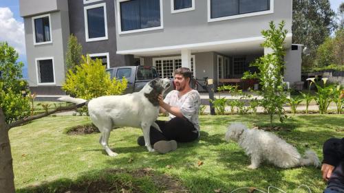 a man sitting on the grass with a sheep and a dog at La Cuadra - Hospedaje en Puembo in Puembo