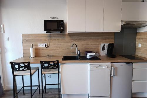 une cuisine avec des placards blancs et un comptoir avec des chaises dans l'établissement Naturiste Cap d'Agde Port Vénus 211, au Cap d'Agde