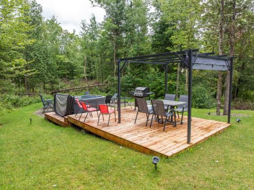 a wooden deck with a grill and chairs at Chalet Escapade, Spa, Piscine in La Patrie