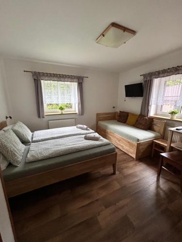 a bedroom with two beds and a couch and two windows at Pension Hones in Horská Kvilda
