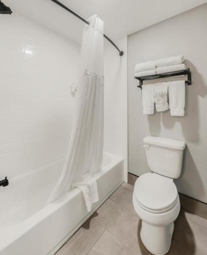 a white bathroom with a toilet and a bath tub at Hawthorn Extended Stay by Wyndham College Station in College Station