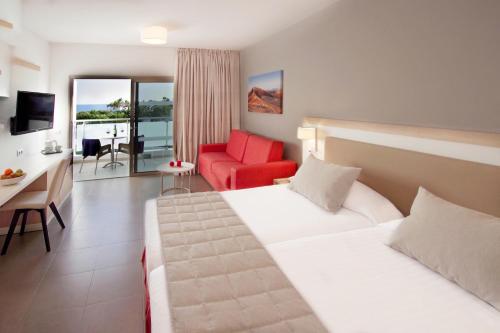 a hotel room with two beds and a red chair at Hotel Lanzarote Village in Puerto del Carmen