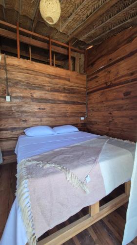 a bed in a room with wooden walls at Puerto Manglar Hostal in Guachaca