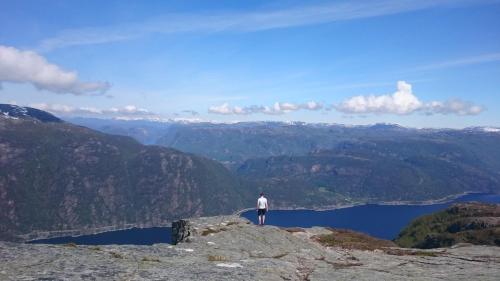 a man standing on top of a mountain overlooking a lake at Koselig feriehus ved fjorden med panorama utsikt in Hjelmeland