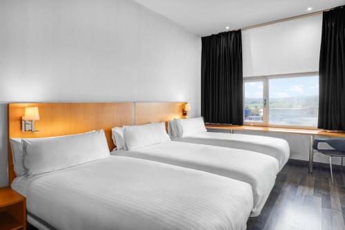 two beds in a hotel room with a window at B&B HOTEL Barcelona Mollet Porta de Gallecs in Mollet del Vallès