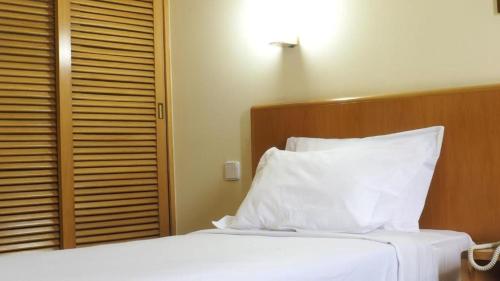 a bedroom with a white bed with a wooden headboard at Flag Hotel Porto Maia in Águas Santas