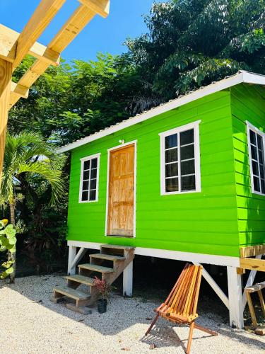 a green tiny house with a wooden door and stairs at Silver Sand, Placencia in Placencia Village