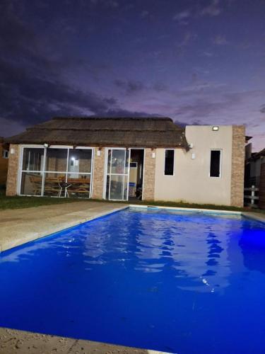 a blue swimming pool in front of a house at Casa 3 dormitorios en Barrio Privado con vigilancia en Haras el Terraplen, General Rodriguez, con Pileta, quincho, parrilla in General Rodríguez