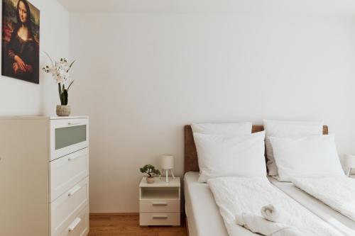a white bedroom with a bed and a dresser at Symphony Apartments Vienna - Garden, Terrace and Grill in Vienna