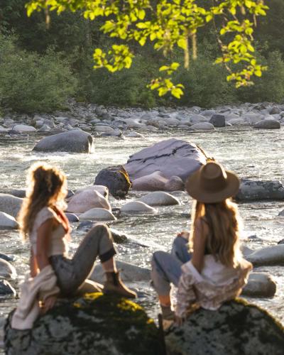 two women sitting on rocks next to a river at Stilly River Haus - Hot tub - Firepit - Fireplace in Granite Falls