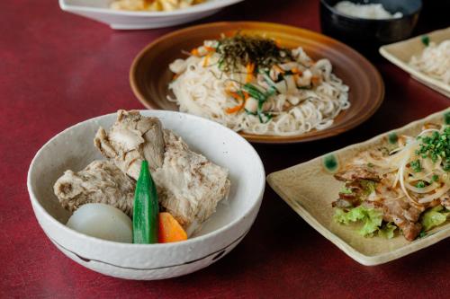 a table with a bowl of food and plates of noodles at Coral Palms in Amami