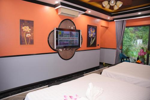 a bedroom with two beds and a tv on the wall at Happy Tam Coc Ecolodge in Ninh Binh