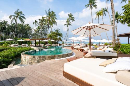 a resort pool with lounge chairs and an umbrella at Nikki Beach Resort & Spa Koh Samui in Lipa Noi