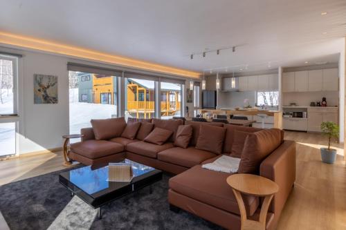 a living room with a brown couch and a kitchen at Tanuki House with spacious living room close to Rusutsu Resort in Rusutsu