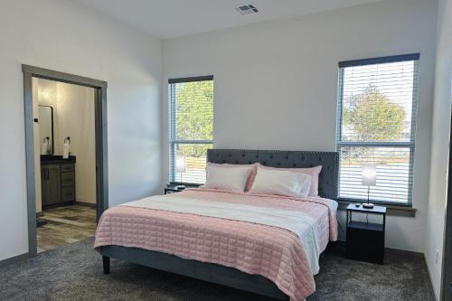 a bedroom with a bed with a pink blanket and two windows at New Cougar Cabin with Air Hockey in Purcell