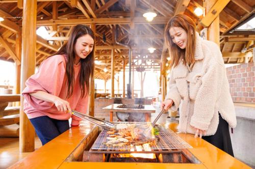 two women cooking food on a grill in a kitchen at Hida-Osaka Fureai no Mori Bungalow in Gero