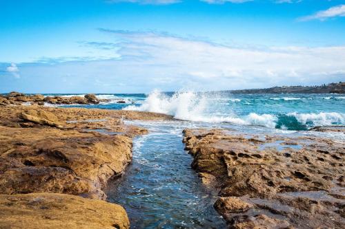 a wave crashing on the shore of a rocky beach at Tranquil Retreat at Caringbah South - Waterfront Ensuite King Room with Spectacular Views in Lilli Pilli