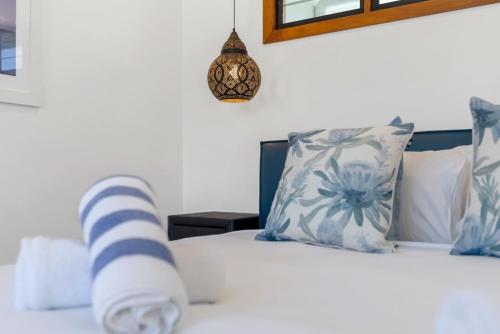 a bed with blue and white pillows and a clock at The Peony Isle - Luxe Lakeside Haven with Pool & Spa in Trinity Beach