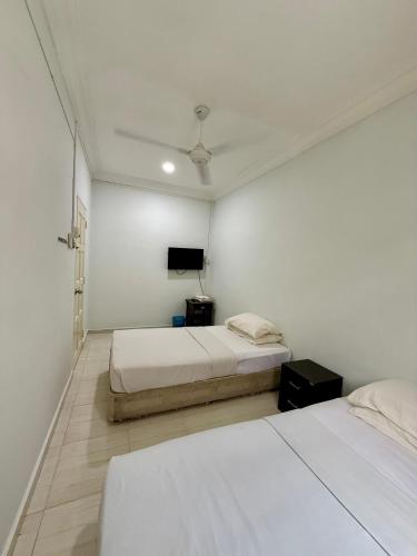 a white room with two beds and a tv at Eco Stay Guesthouse in Kuantan