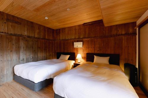 two beds in a room with wooden walls at NIPPONIA HOTEL 伊賀上野 城下町 in Iga