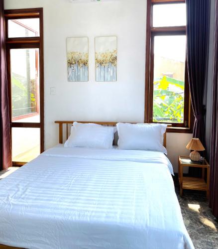 a bedroom with a large white bed with two windows at Vang's Homestay - Huế in Ấp Long Hồ Hạ